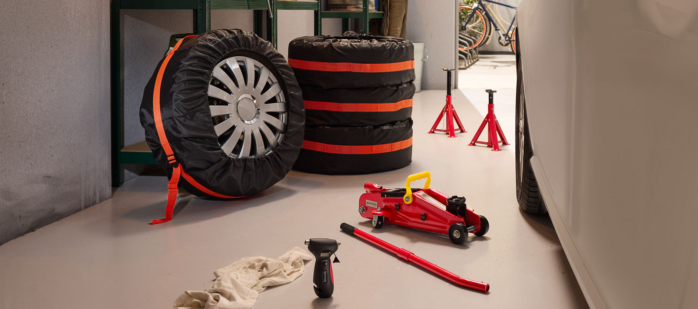 Car tires with covers, a jack, and stands in a garage.