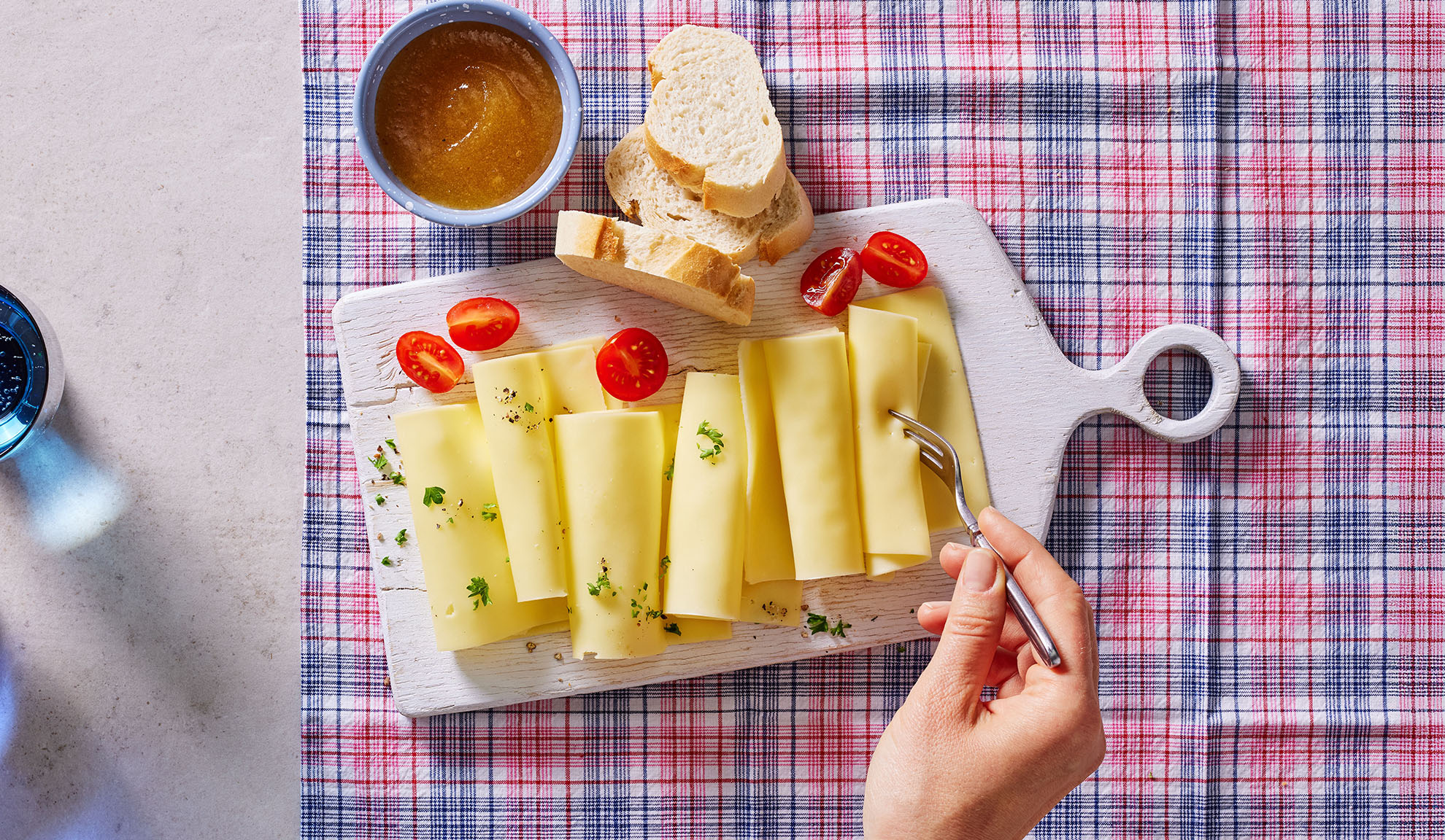 Cheese slices, cherry tomatoes, bread, and jam on a serving board.