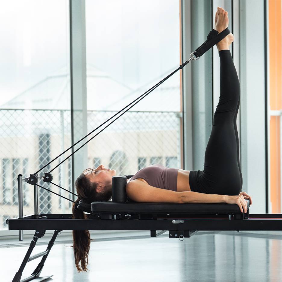 Woman doing a leg exercise on a Pilates reformer machine.