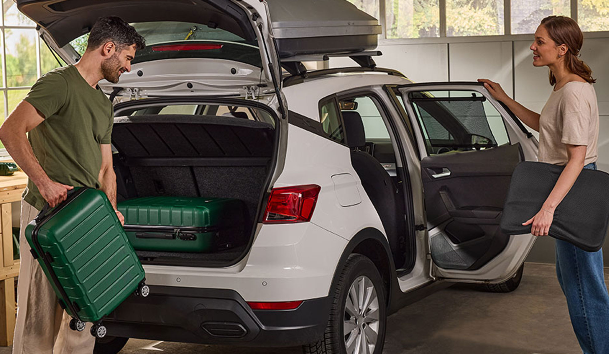 Couple packing luggage and car accessories into a white SUV for a trip.