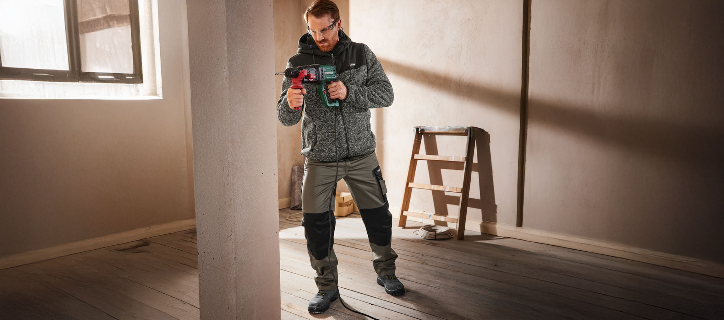 Man in workwear drilling into a wall with a power drill.