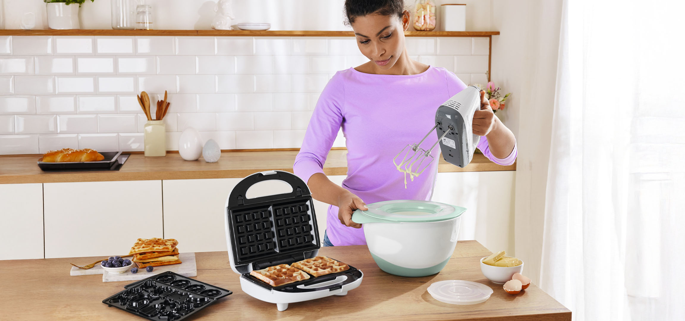 Woman making waffles and donuts with a waffle maker and a hand mixer.