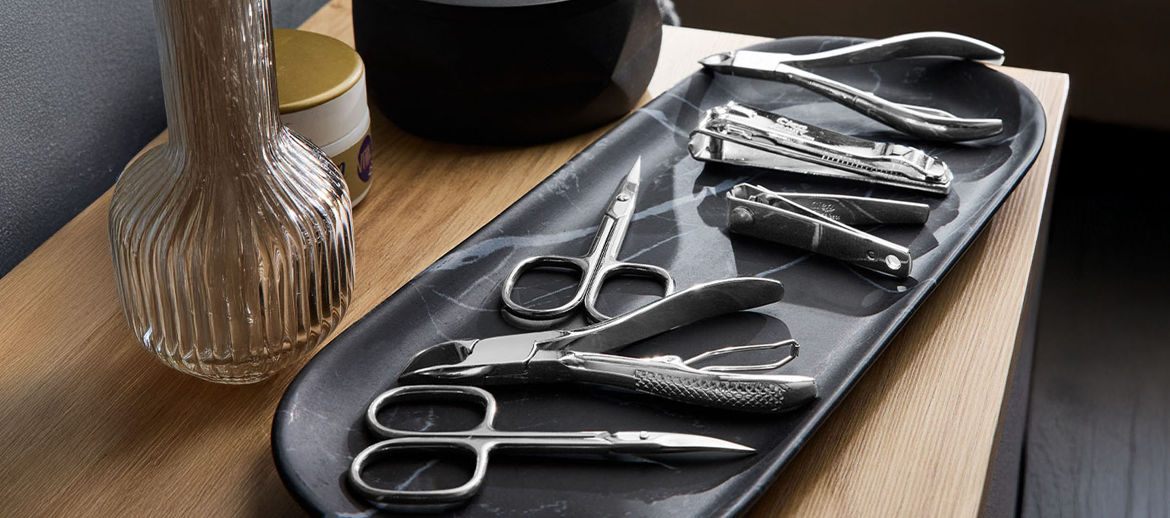 Manicure and pedicure tools on a marble tray, with a vase and jar in the background.