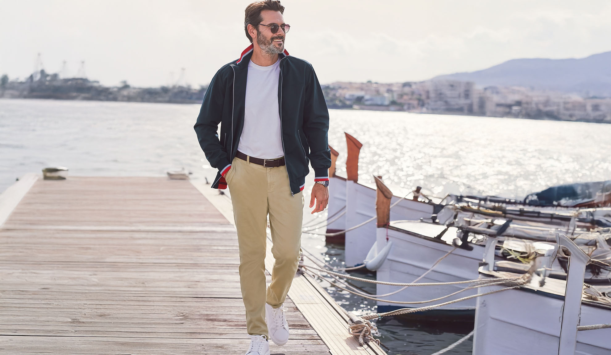 Man in a navy jacket, white t-shirt, and khaki pants on a pier.