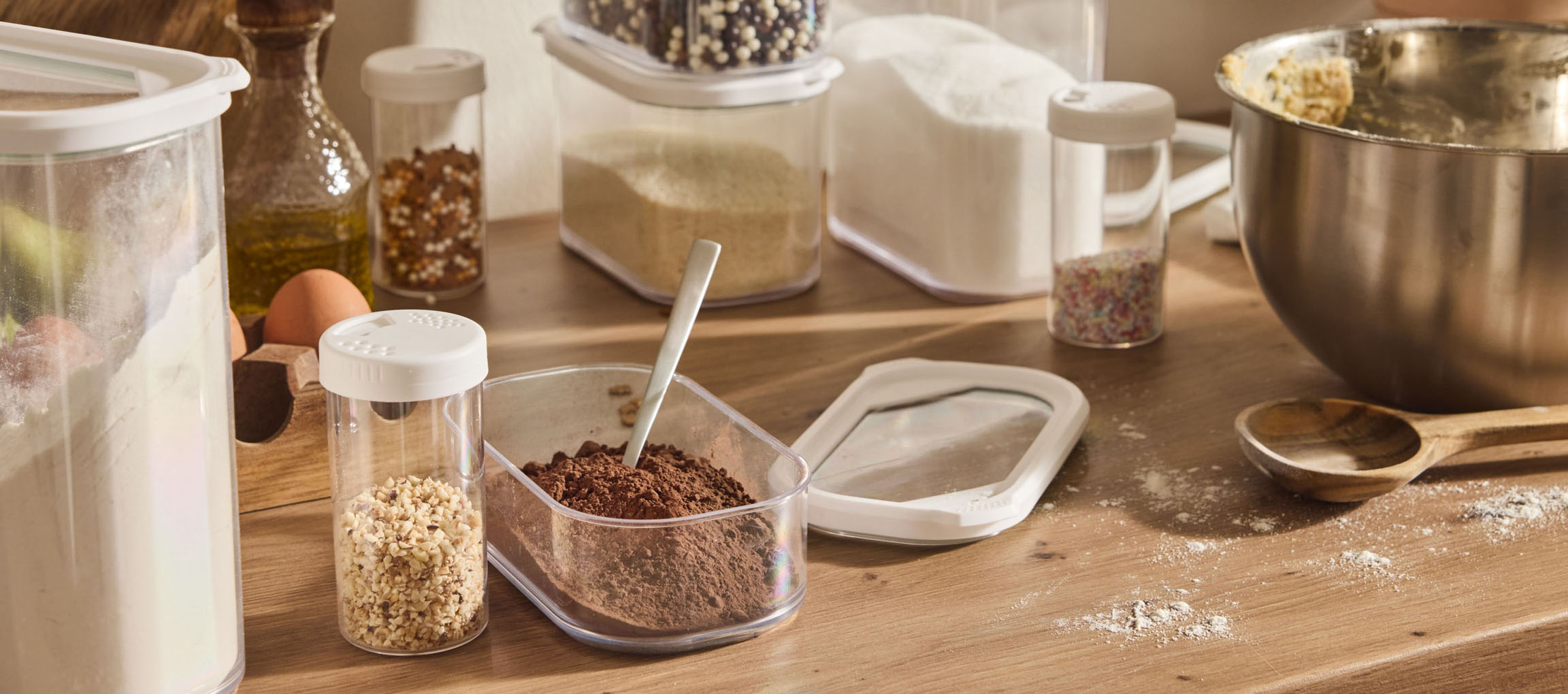 Baking ingredients in clear plastic containers, with flour, sugar, cocoa, and eggs.