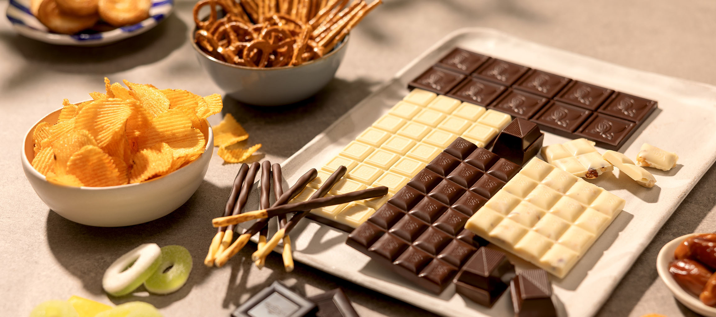 Assorted chocolates, potato chips, pretzels, and candies on a table.