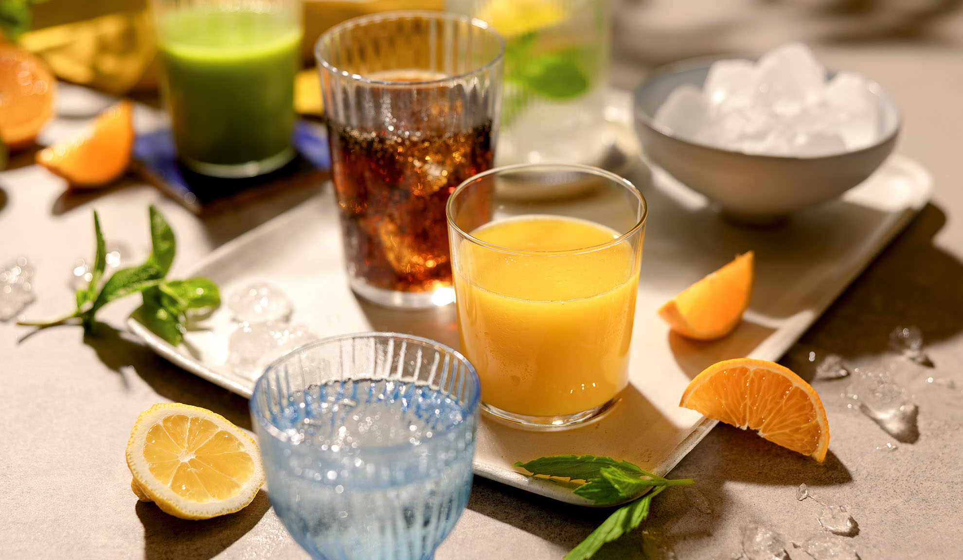 Various refreshing drinks with ice, citrus slices, and mint on a tray.