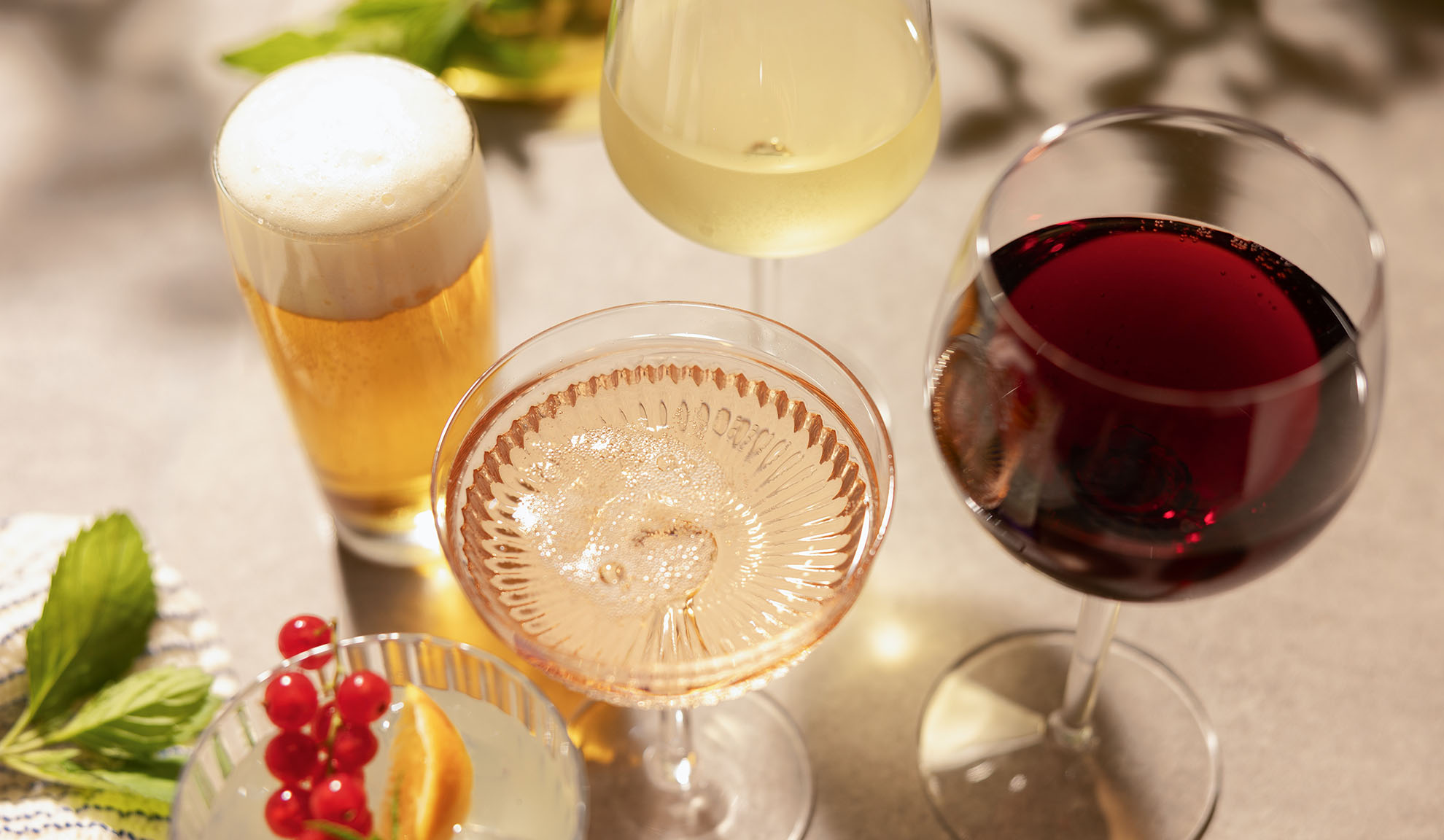 Glasses of beer, white, rosé, and red wine, with a cocktail and berries.