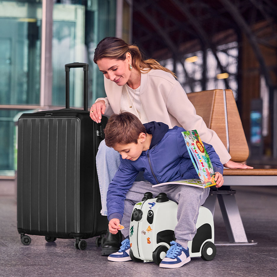 Woman and child with large black suitcase and panda ride-on suitcase at an airport.