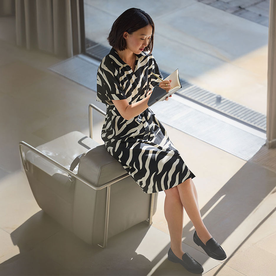 Woman in a zebra print dress and loafers, writing in a notebook.