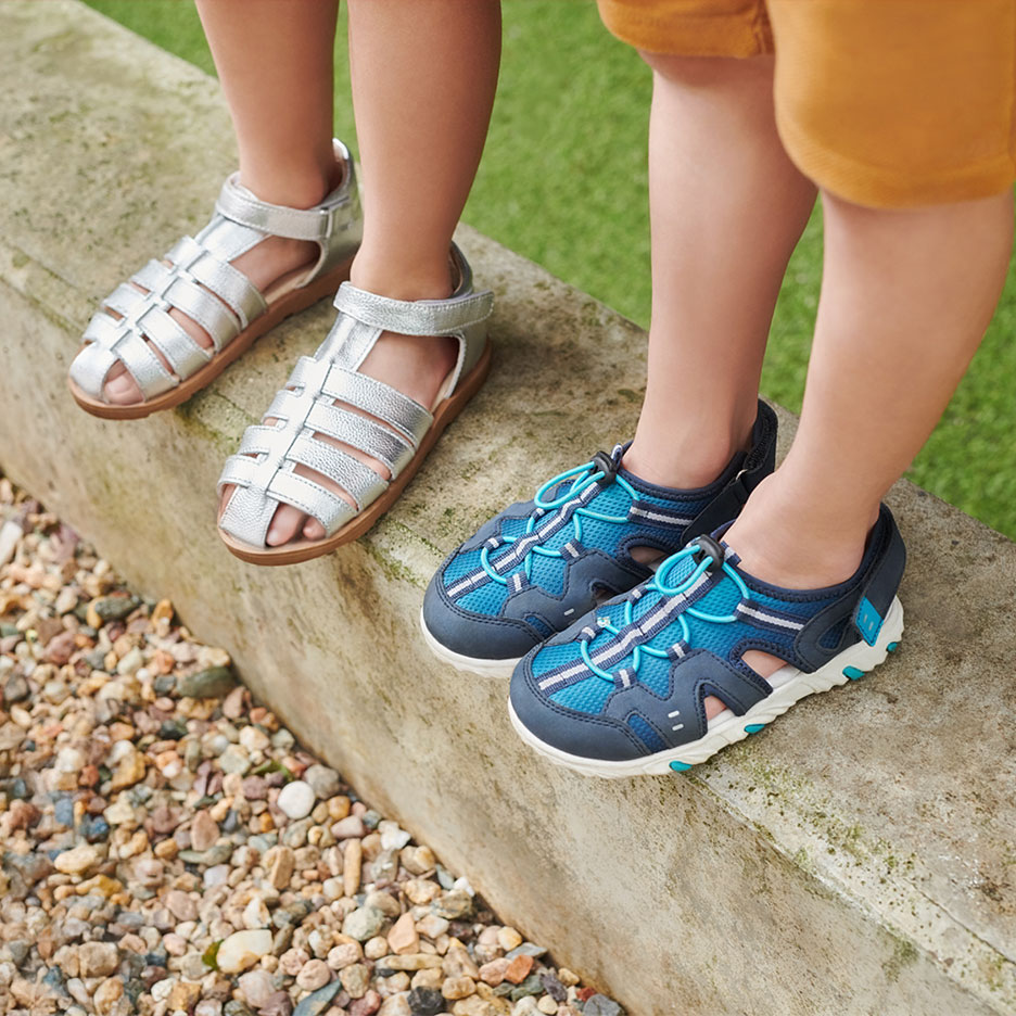 Two pairs of children's sandals: silver and blue, on a curb.