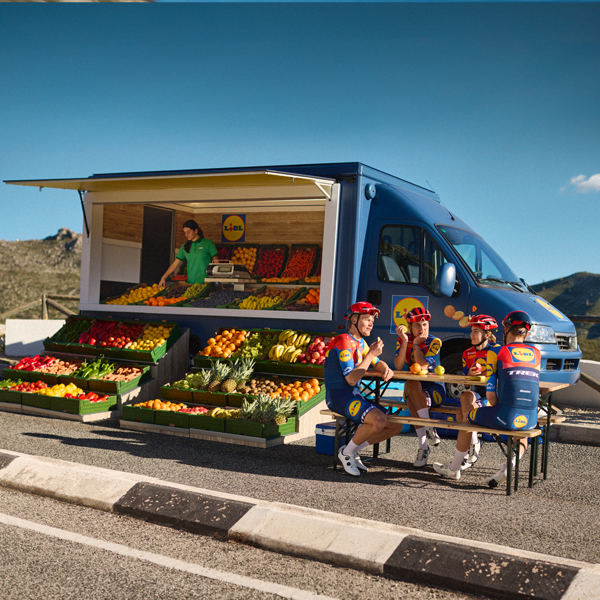 Cyclists take a break at a Lidl truck stocked with fresh produce.