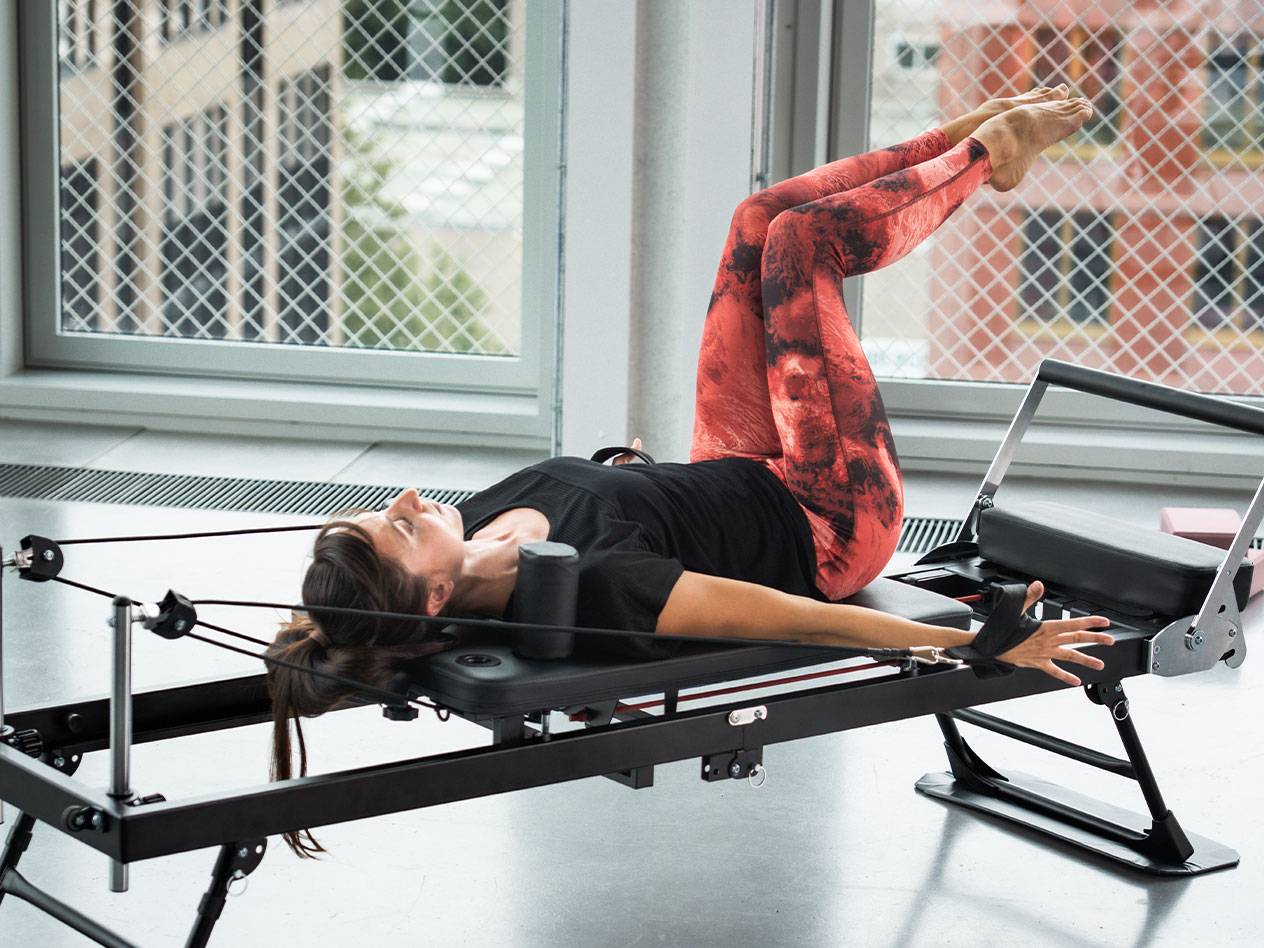 Woman doing Pilates on a reformer machine, in red and black leggings