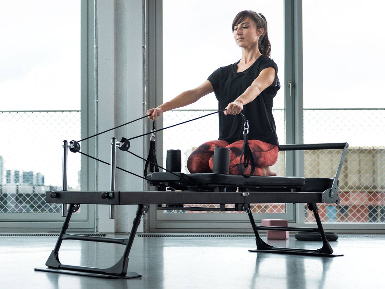 Woman doing Pilates on a reformer machine with large windows in the background.