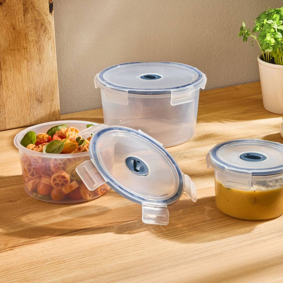 Clear round food containers with blue-rimmed lids, one filled with pasta salad, another with soup.