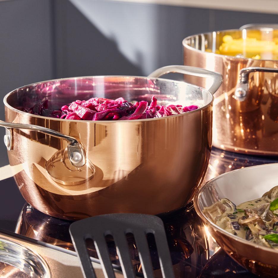 Copper pots with red cabbage and pasta on a hob, with a bowl of mushroom stew.