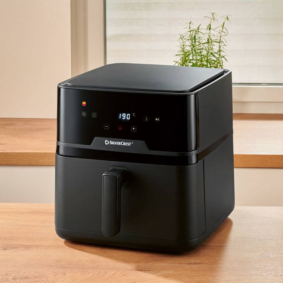 Black digital air fryer on a wooden table, with 190 °C displayed.