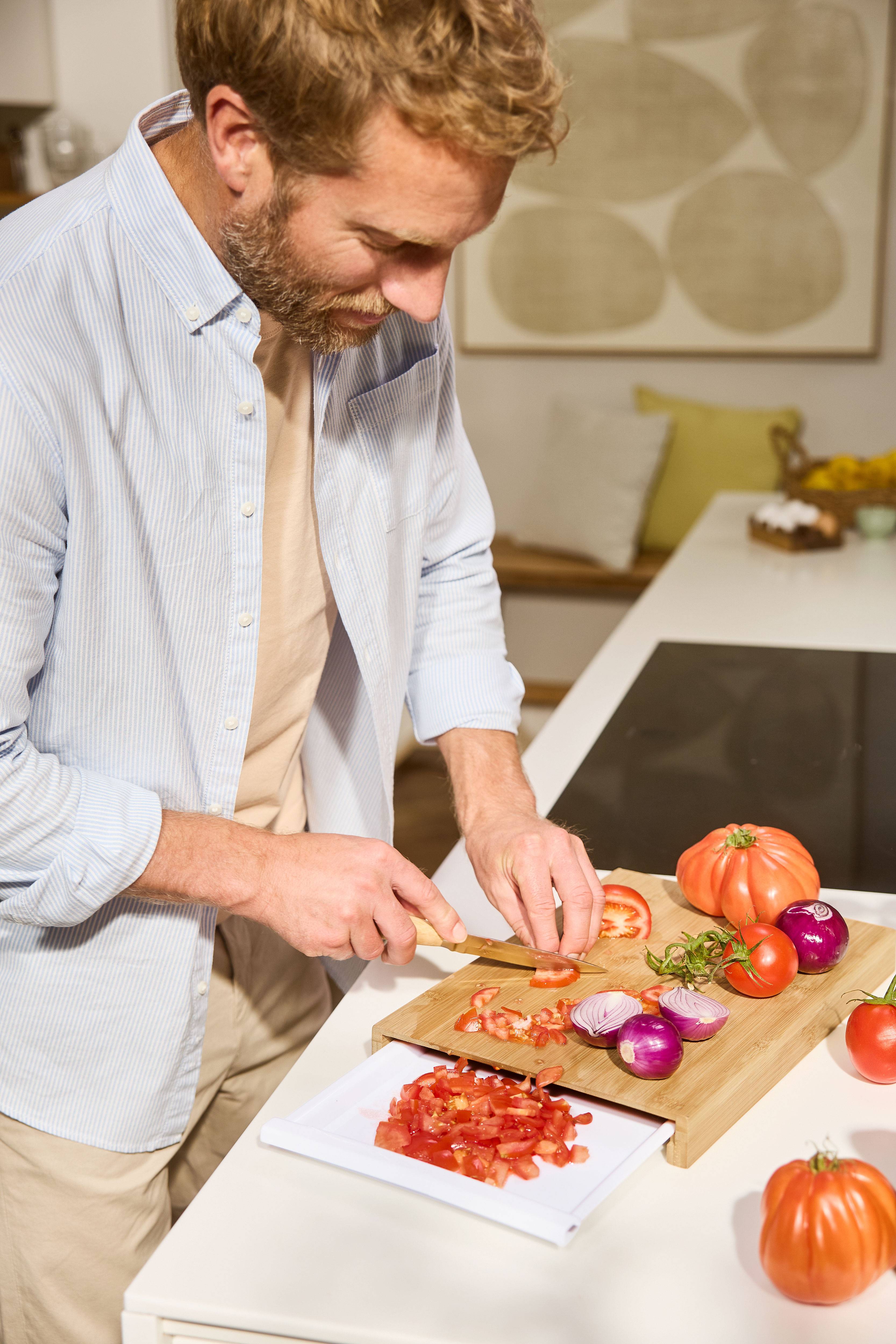 Man chopping tomatoes and onions on a wooden cutting board in the kitchen.