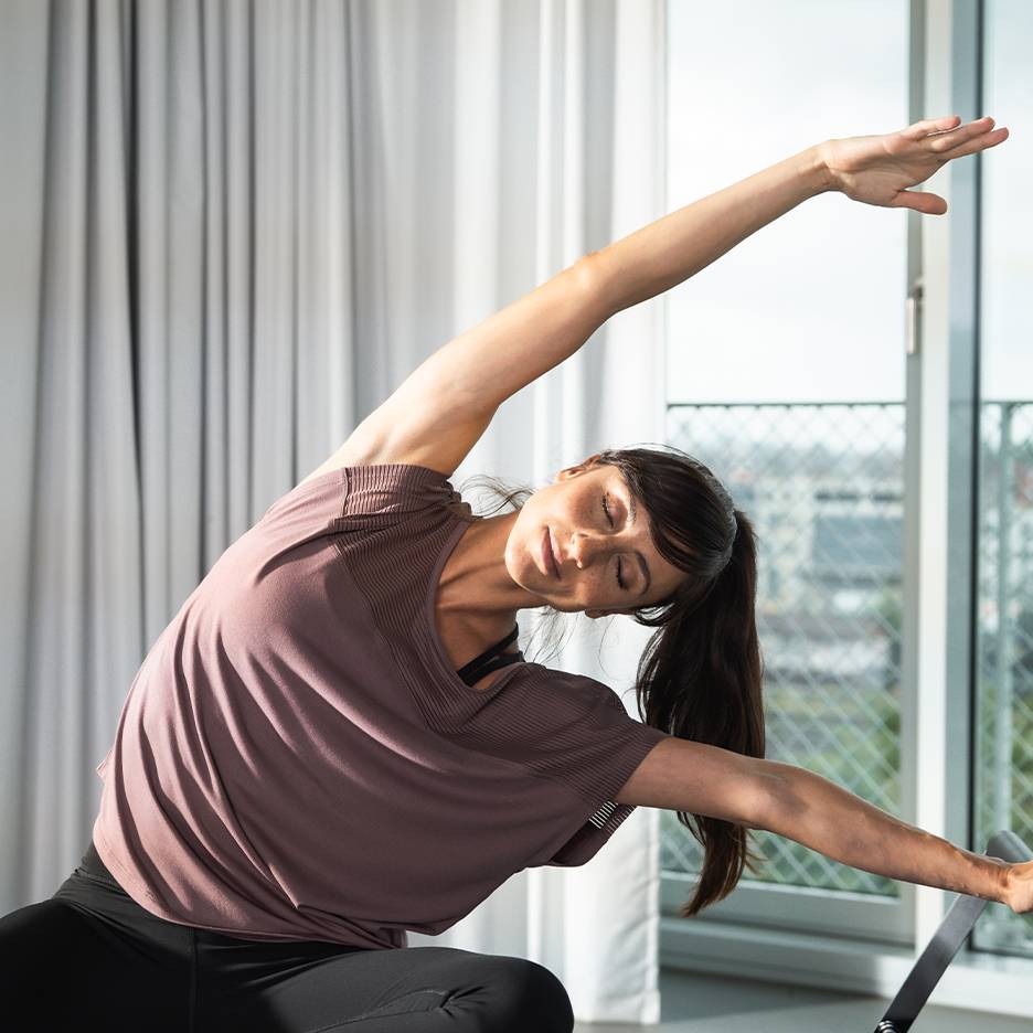 Woman exercising in a sports t-shirt and black leggings, stretching with closed eyes.