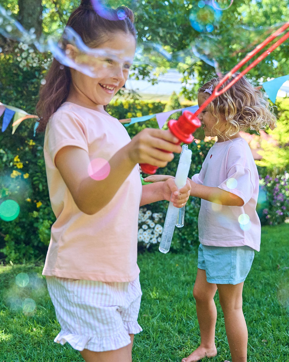 Two girls play with bubbles in the garden, wearing summer clothes.