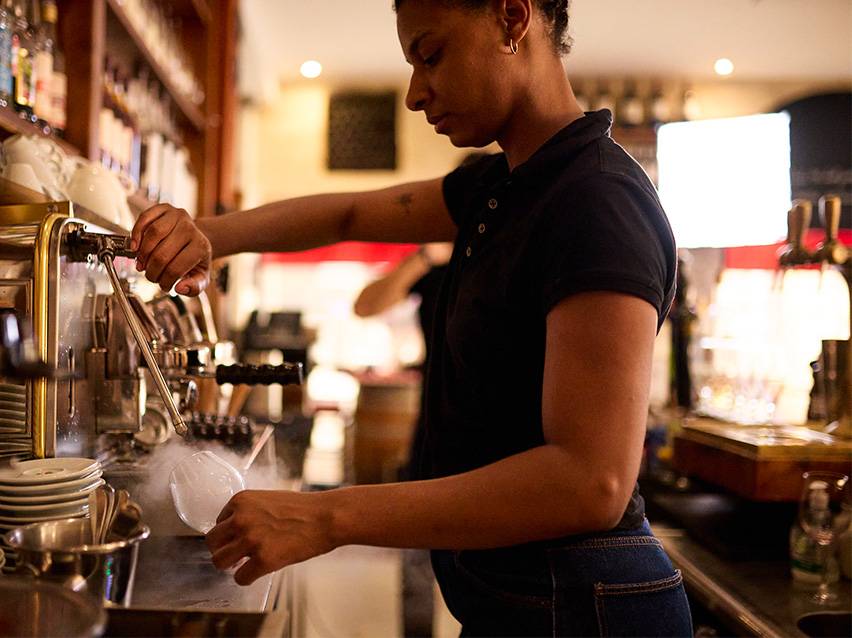 Barista preparing a drink with steam from an espresso machine.