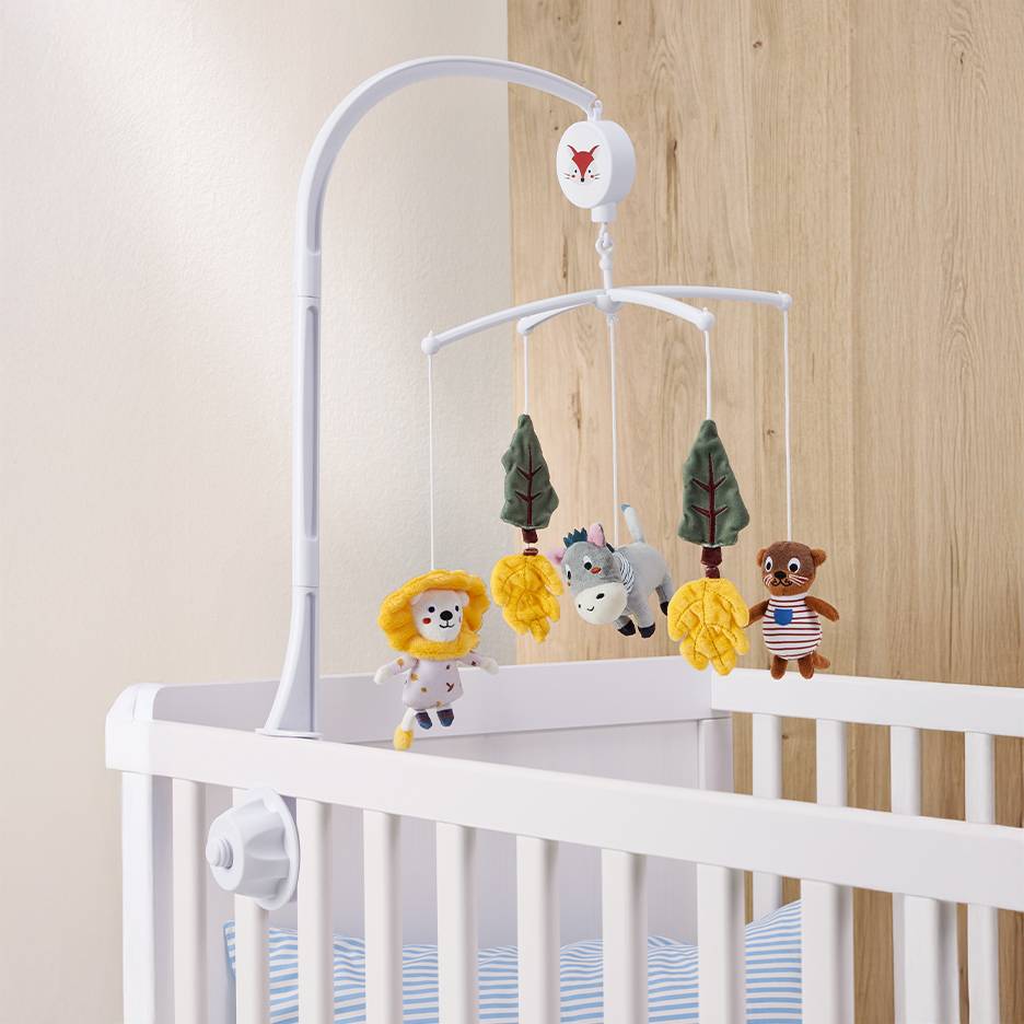 White baby crib with a mobile featuring animal and tree toys.