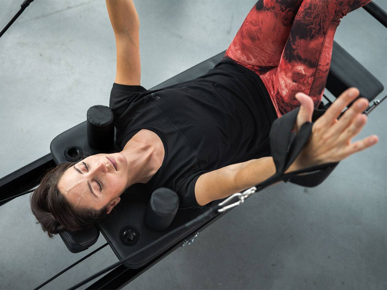 Woman in activewear lying on a Pilates reformer, exercising.