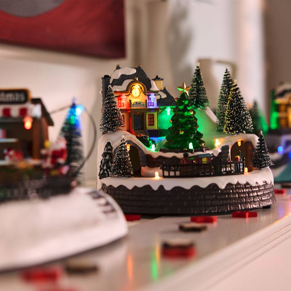 Christmas village with illuminated station, trees, and miniature railway.