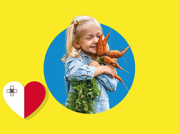 Smiling child holding carrots, with a Maltese flag heart on a yellow background.