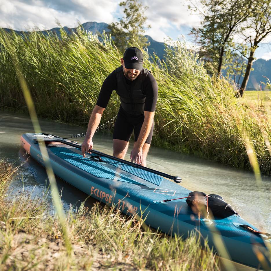 Man in black wetsuit preparing for paddleboard, board in water