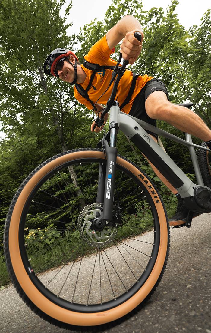 A man rides a grey Maxxis e-bike through a forest.