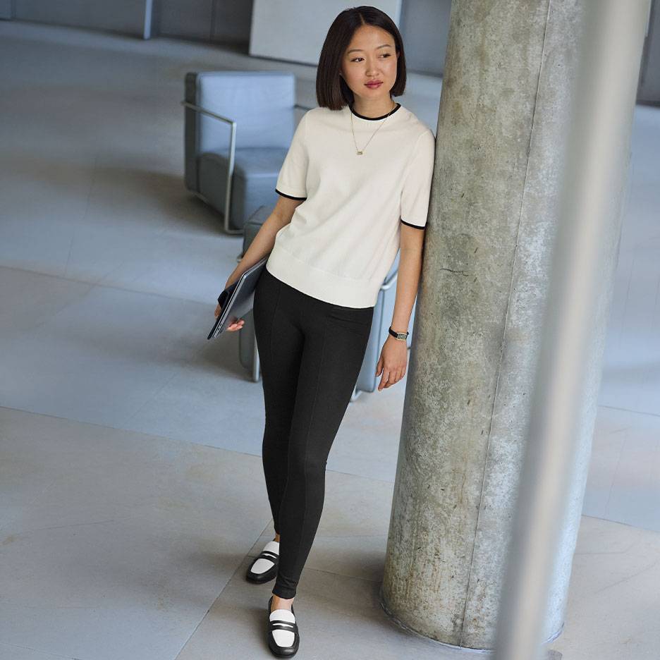 Woman in a white short-sleeved top with black trim, black leggings, and two-tone loafers.