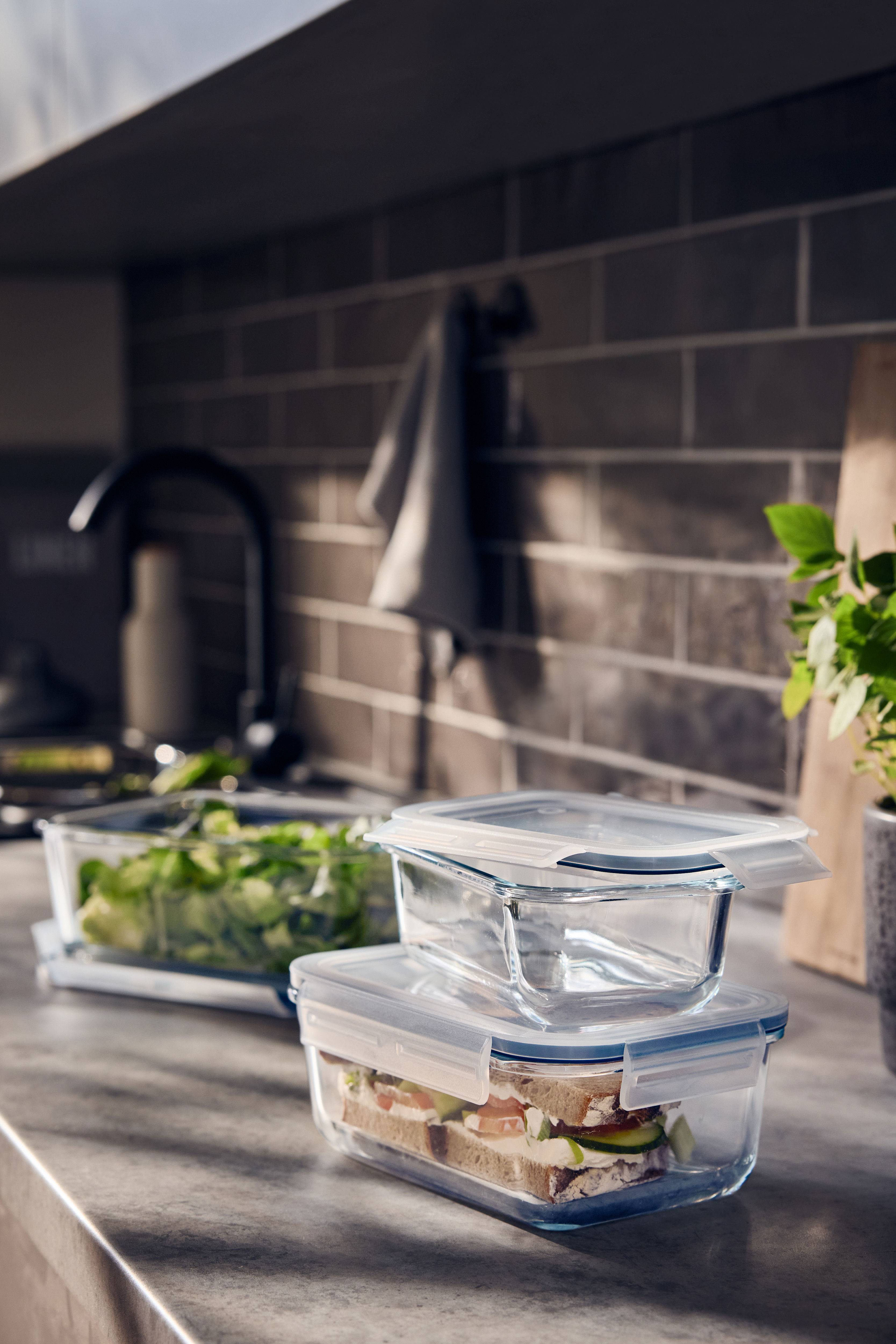 Glass containers with lids, one with a sandwich and one with salad, in a kitchen.