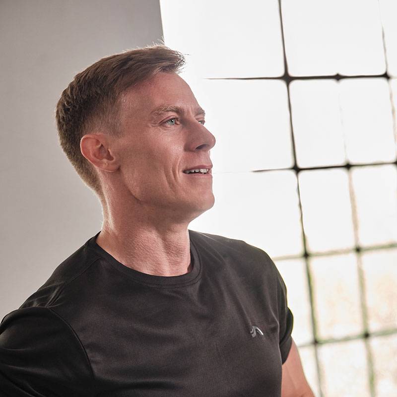 A man in a black t-shirt looks away towards a window.