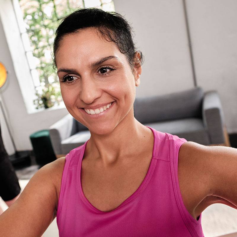 Smiling woman in pink tank top exercising at home.