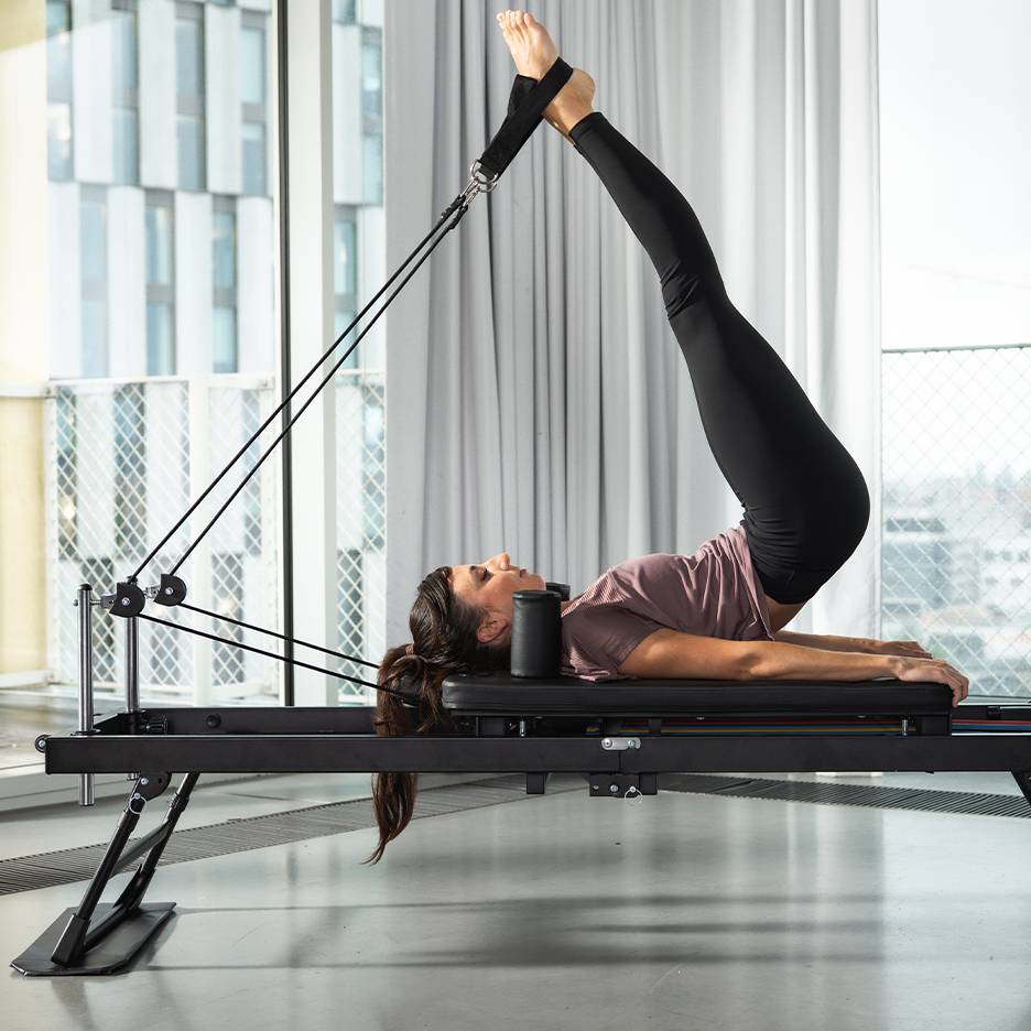 Woman exercising Pilates on a black Pilates machine with legs up.