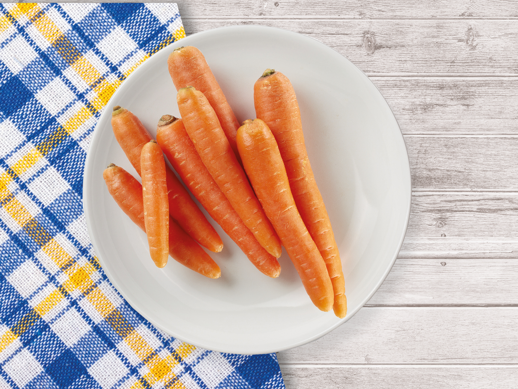 A plate of fresh carrots sits on a blue and yellow checkered tablecloth.