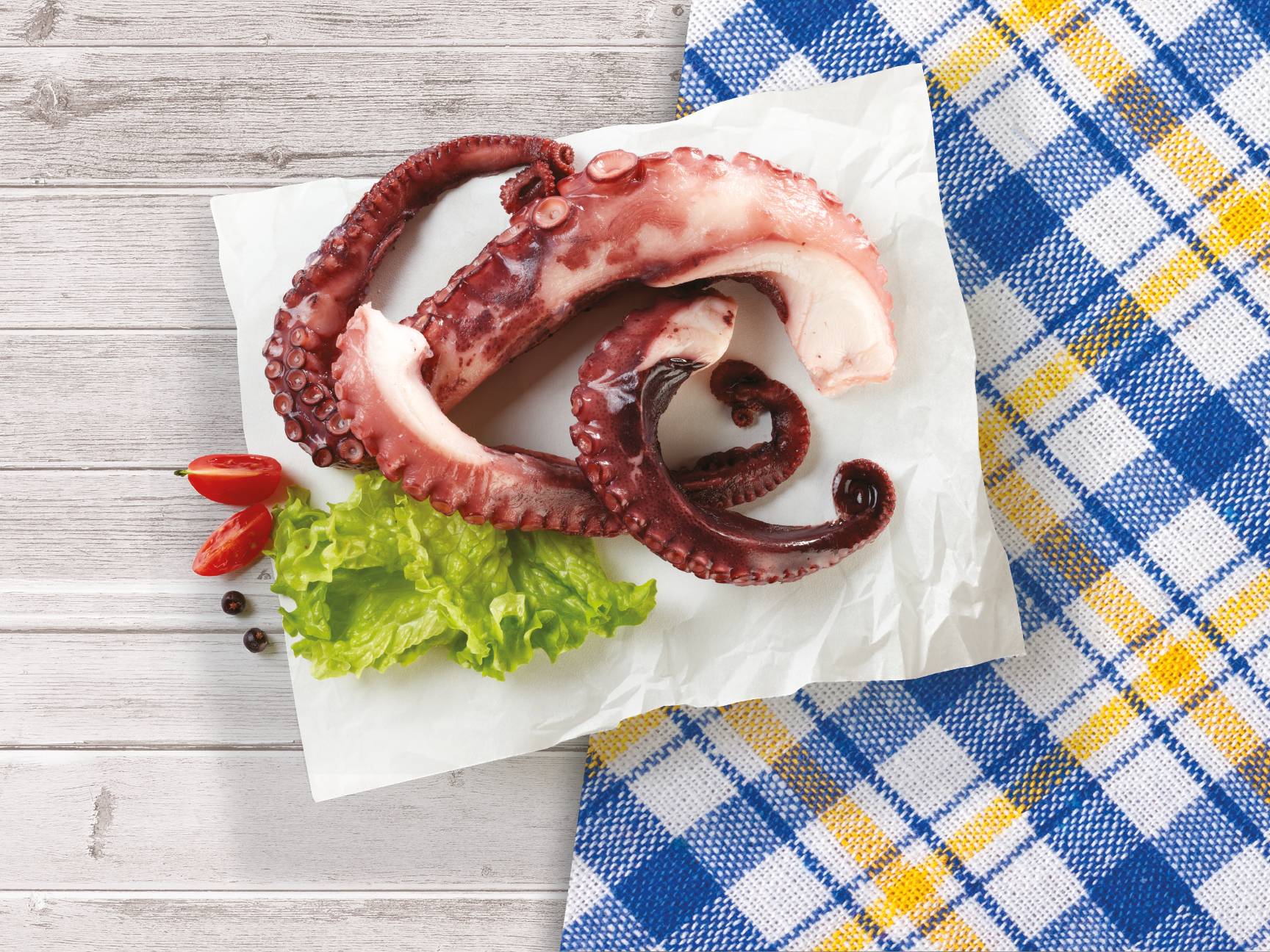 Prepared octopus tentacles on parchment paper with lettuce and cherry tomatoes.