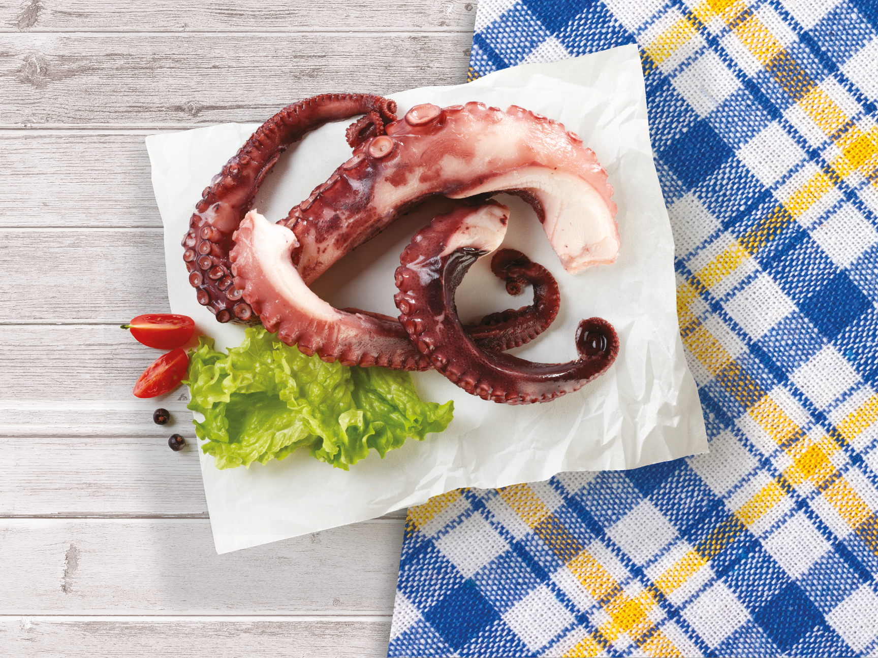 Prepared octopus tentacles on parchment paper with lettuce and cherry tomatoes.