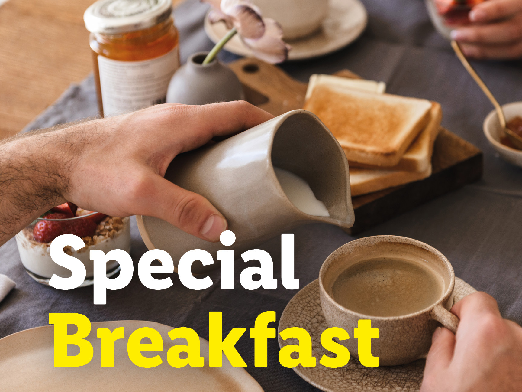 A person pouring milk into coffee at a breakfast table with toast and jam.