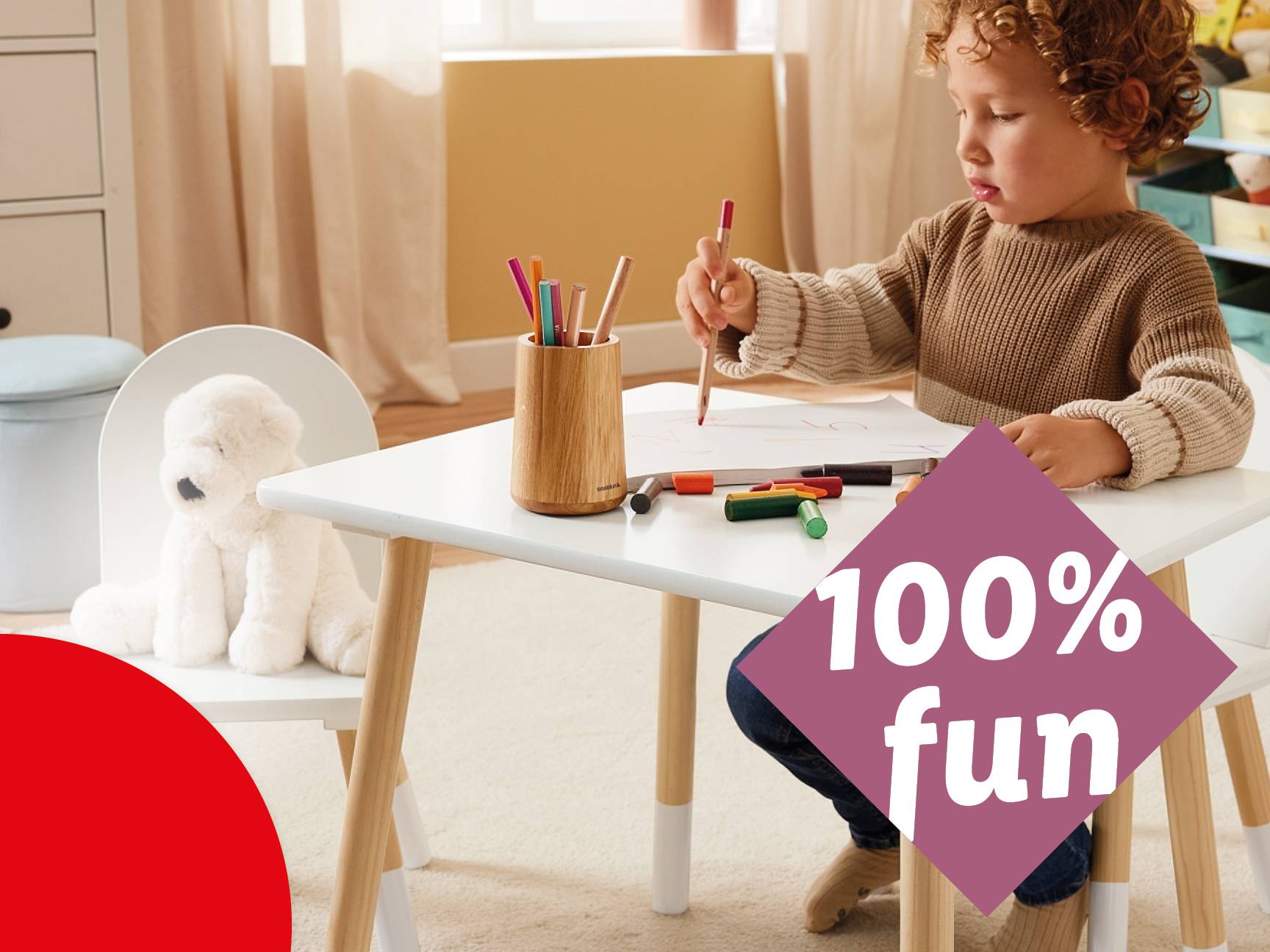 A young boy drawing at a white and wood children's table with a pencil holder and crayons.