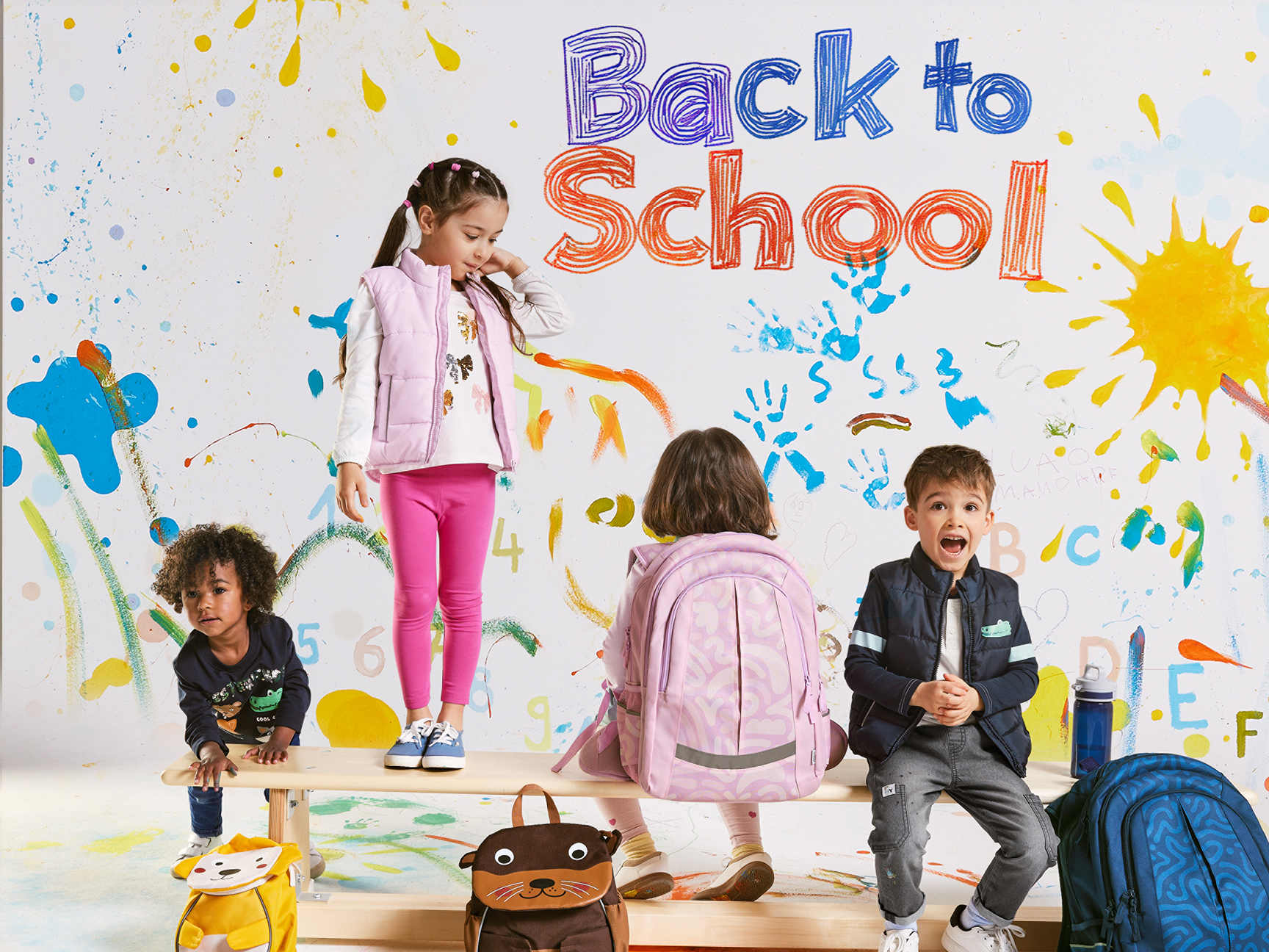 Kids with backpacks and school supplies in a colorful, painted room.