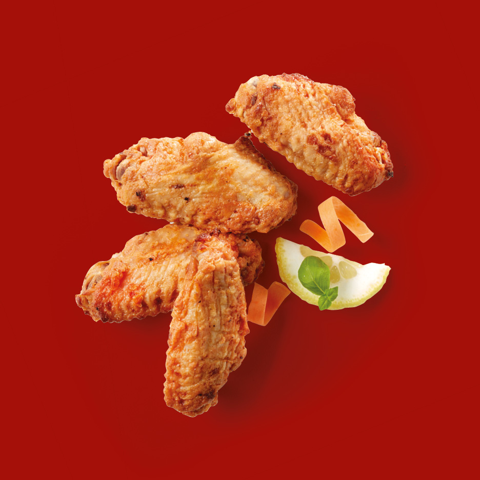 Crispy fried chicken wings with lemon and carrot garnish on a red background.