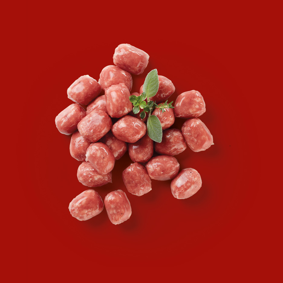 Small raw sausages with herbs on a red background