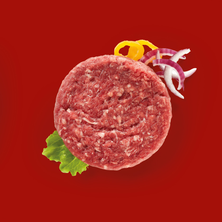 Raw beef burger patty with lettuce, red onion, and yellow bell pepper on red background.