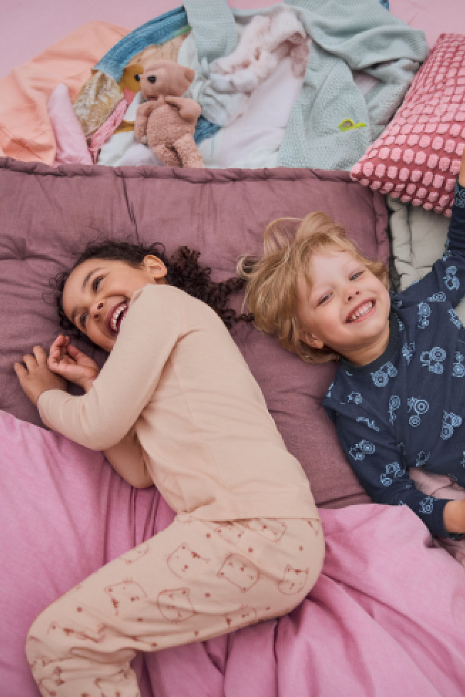 Two happy children in pajamas lying on a bed with colorful bedding and clothes.