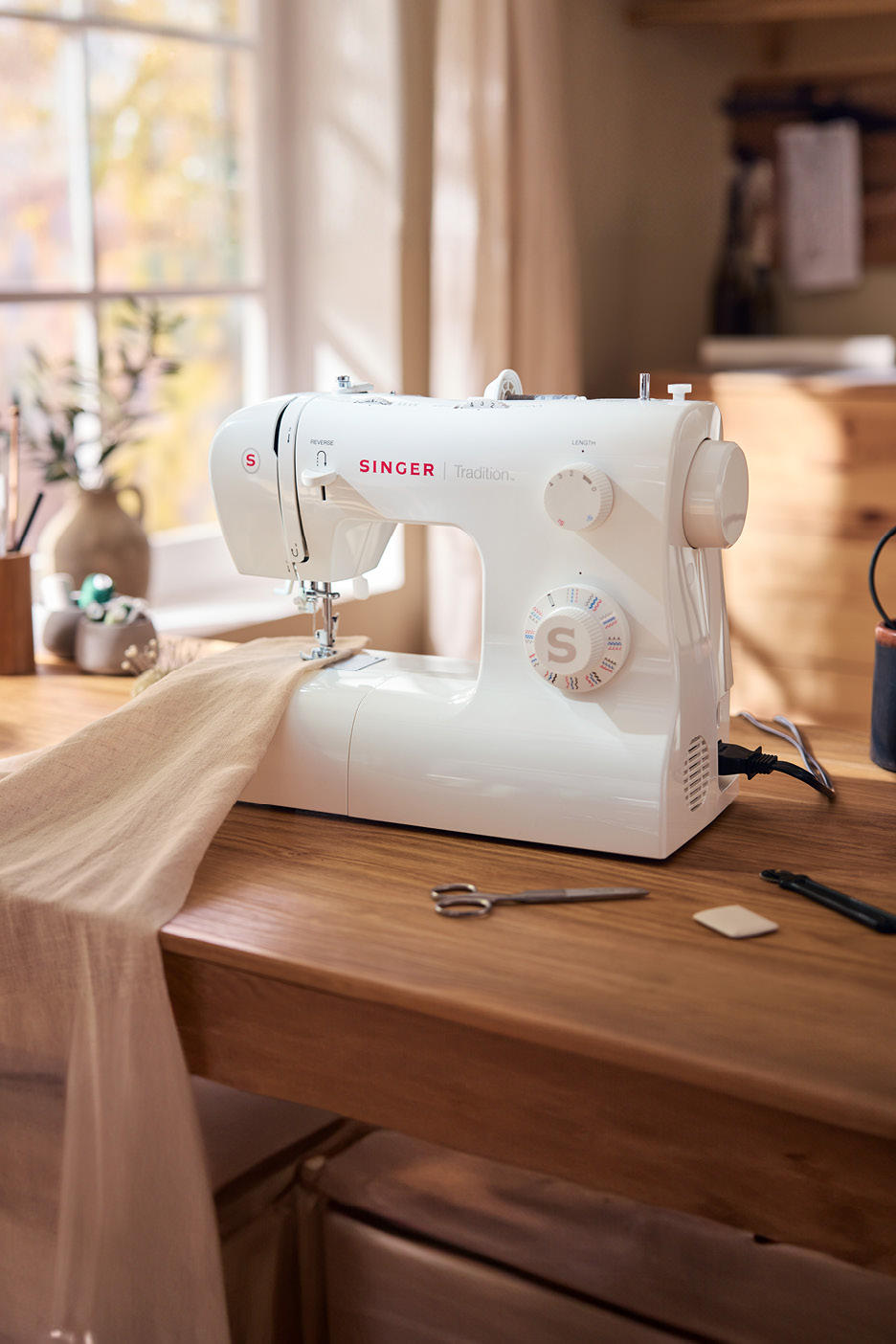 White SINGER Tradition sewing machine on a wooden table with fabric and sewing tools.