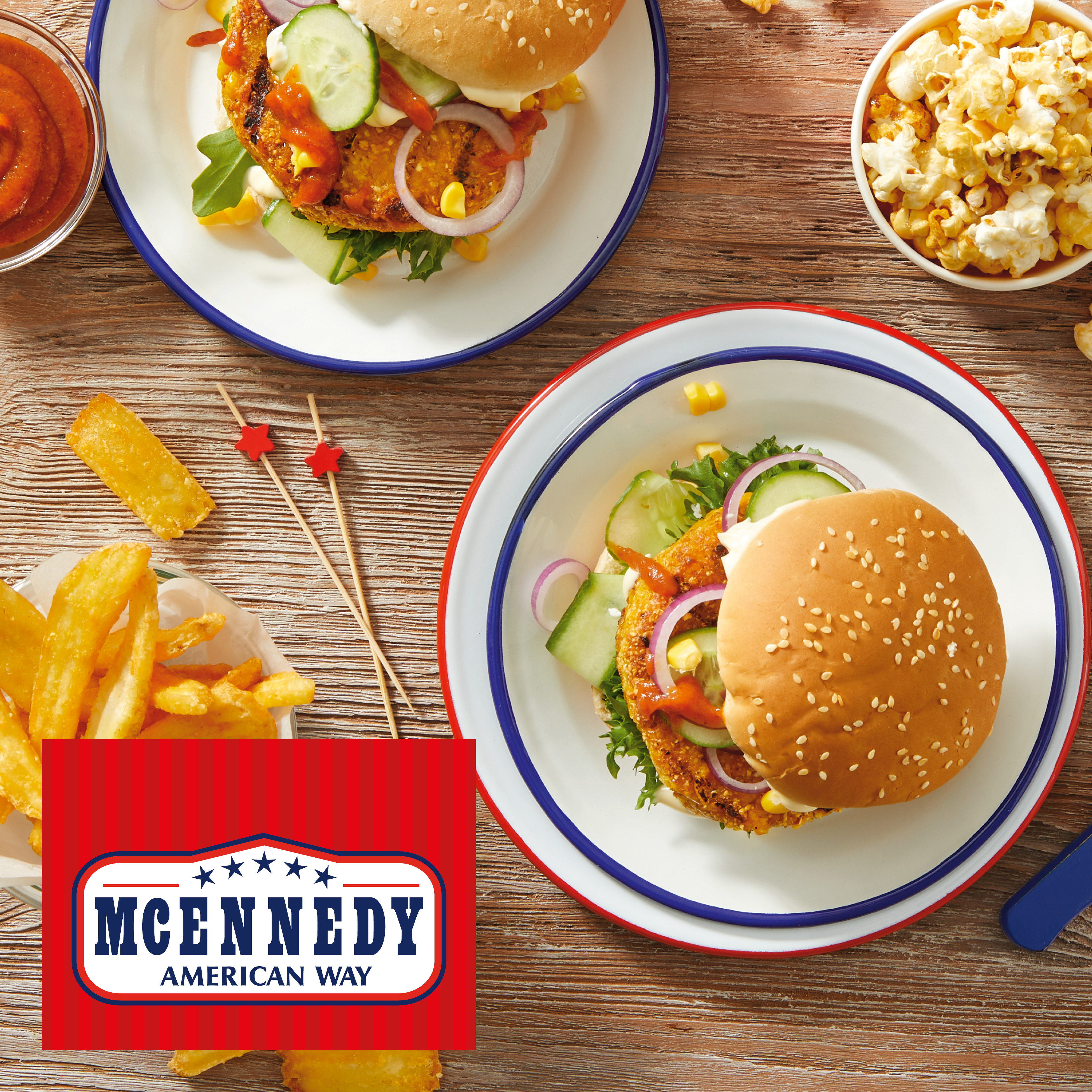 Two burgers with fries, popcorn, and sauce on a wooden table, with an American-themed logo.
