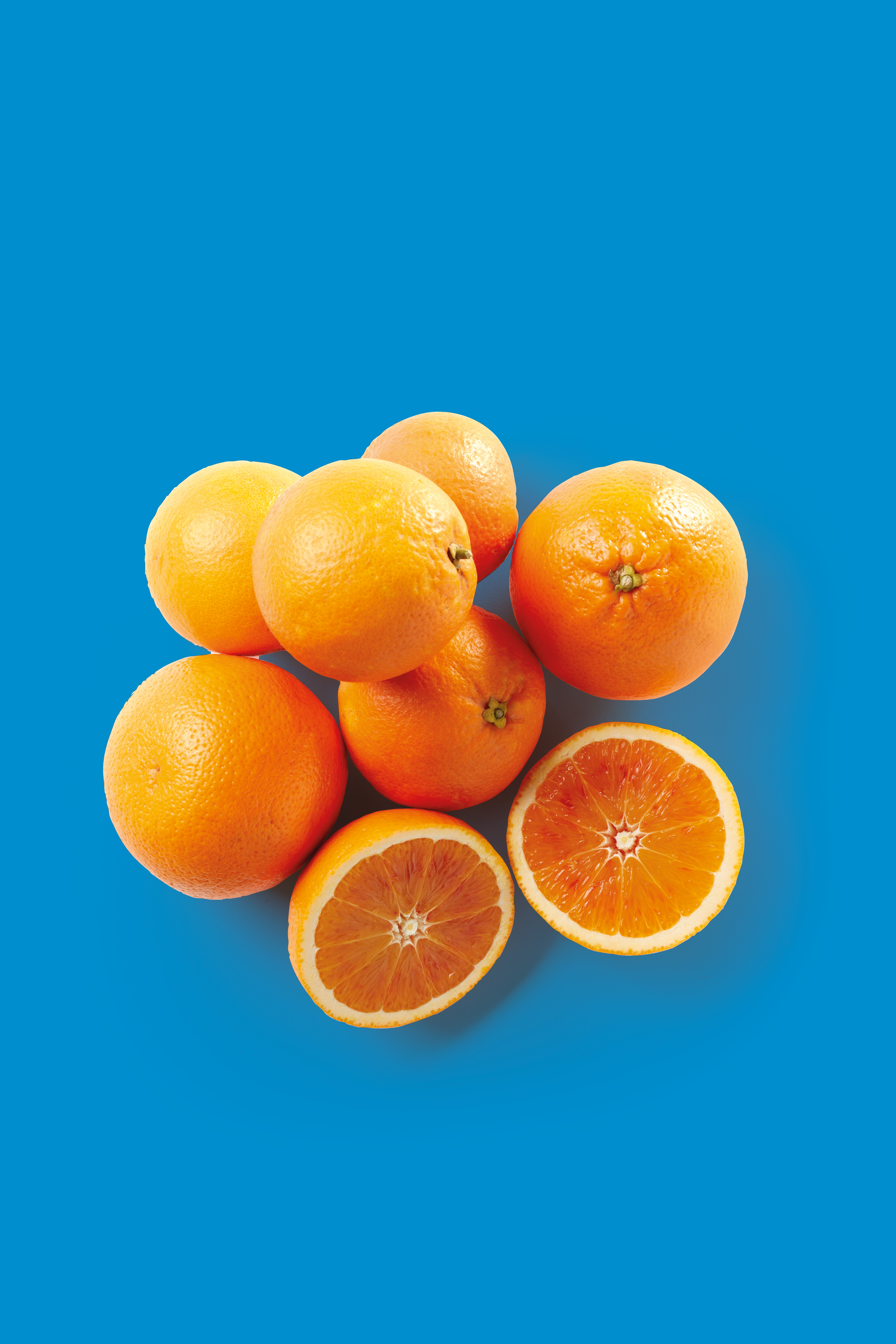 A group of whole and halved oranges on a vibrant blue background.