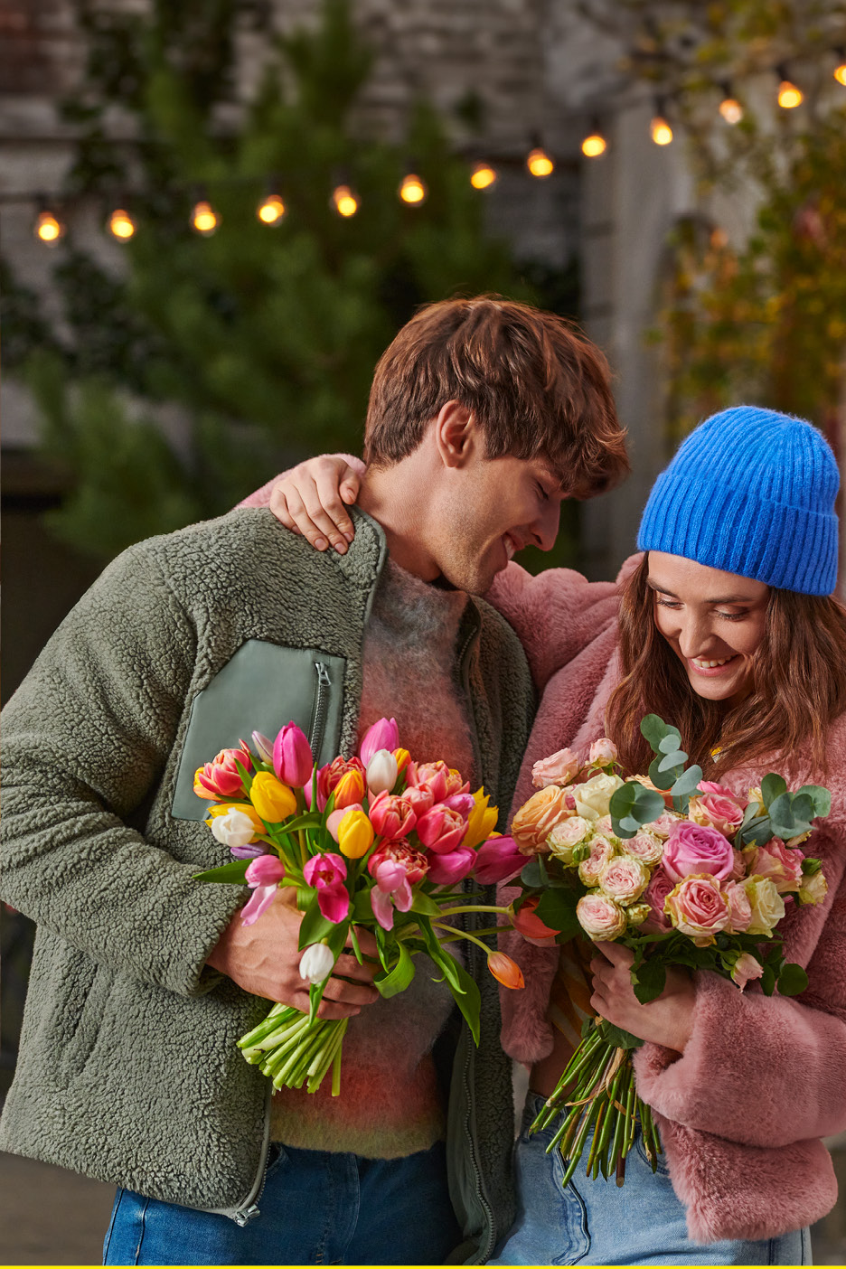 A couple holding bouquets of colorful tulips and roses, smiling at each other.